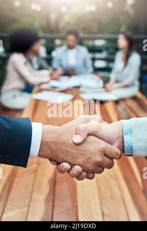 Bringen wir gemeinsam mehr Erfolg auf den Tisch. Nahaufnahme von zwei nicht erkennbaren Geschäftsleuten, die sich im Hintergrund mit ihren Kollegen die Hände schüttelten. Stockfoto