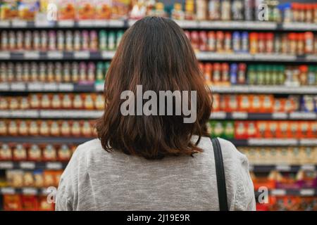Die besten Produkte zum besten Preis zu finden. Rückansicht einer Frau, die in einem Lebensmittelgeschäft nach Gegenständen browsen soll. Stockfoto