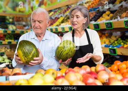 Dame im Gemüsehändler hilft dem alten Mann, Melone zu wählen Stockfoto