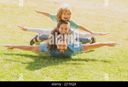 Familie liegt auf Gras im Park. Fly-Konzept, kleiner Junge sitzt Pickaback, während der Flug imitiert. Stockfoto