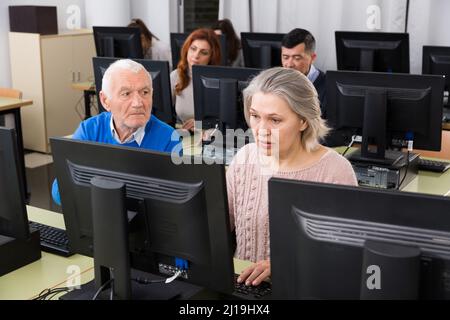 Junge und reife Kollegen sitzen und arbeiten an Computern Stockfoto