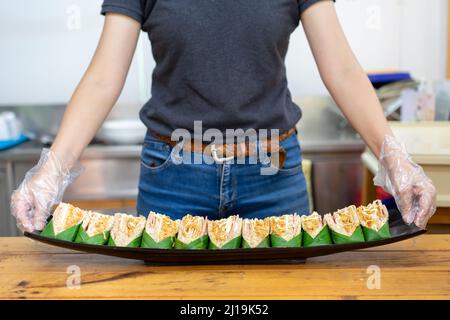 Getrocknete Schweinebandwiches werden auf der schwarzen Bootschüssel-Form von einer asiatischen jungen Frau mit Plastikhandschuhen angeordnet. Stockfoto