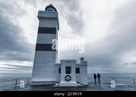 Alter Leuchtturm Garoskagi, Gardskagi, junges Paar mit Blick auf das Meer, Abendhimmel, Hintergrundbeleuchtung, Gardur, Suournes, Sudurnes, Reykjanes Peninsula, in der Nähe Stockfoto