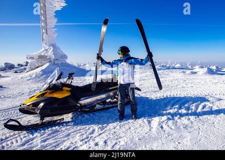 Transfer Tour des Athleten Skifahrer auf dem Schneemobil auf den Gipfel des Berges für Abfahrt auf Neuschnee. Stockfoto