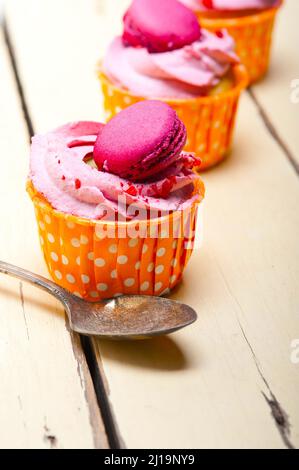 Frischer rosa Beerencreme-Cupcake mit Makronen auf dem rustikalen Holztisch Stockfoto