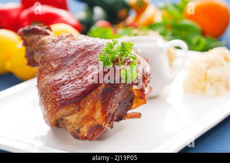 Original deutsches BBQ Schweinshaxe serviert mit Kartoffelpüree und Sauerkraut, frisches Gemüse auf dem Hintergrund Stockfoto