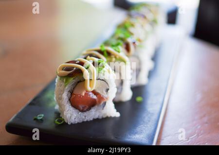 California Rolls Maki Sushi Roll mit rohem Lachs Thunfisch Avocado Ei Apfel grüne Zwiebel auf schwarzem Teller Stockfoto