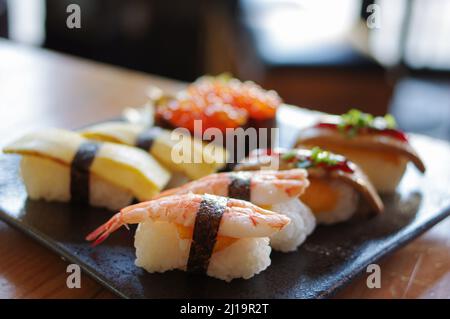 Ikura Sushi und Foie Gras, Tamago, Shrimp Nigiri auf schwarzem Teller Stockfoto