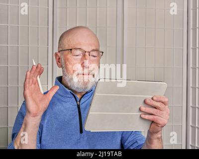 Ein lächelnder Senior liest, schaut sich etwas an oder chattet online mit einem digitalen Tablet Stockfoto