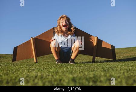 Kind, das im Flugzeug fliegt, machte Handwerk aus Pappflügeln. Traum, Phantasie, Kindheit. Reise- und Sommerurlaubskonzept. Lächelndes Kind, das davon träumt Stockfoto
