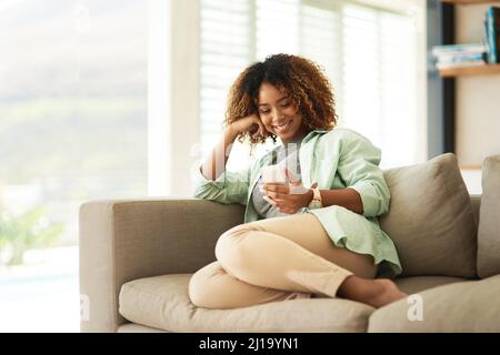 Einige Texte können Ihren Tag einfach aufhellen. Eine attraktive junge Frau, die ihr Handy benutzt, während sie sich zu Hause auf dem Sofa entspannt. Stockfoto