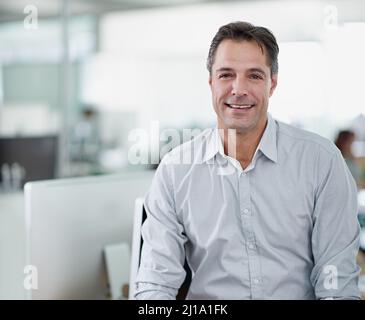 HES hat einen einfachen Führungsstil. Porträt eines reifen Geschäftsmannes, der auf seinem Schreibtisch sitzt. Stockfoto