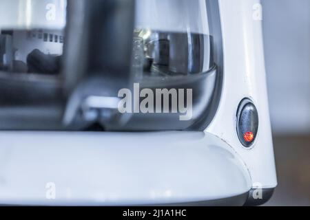 Nahaufnahme einer Kaffeemaschine mit weißem Filter, Glaskanne und schwarzem Kunststoffgriff, eingeschaltet mit Kaffee in einer Küche, Deutschland Stockfoto