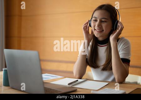 Lächelnd asiatische Mädchen Student tragen drahtlose Kopfhörer Studie online, glücklich junge Frau lernen Sprache hören Vortrag sehen Webinar schreiben Notizen ansehen Stockfoto