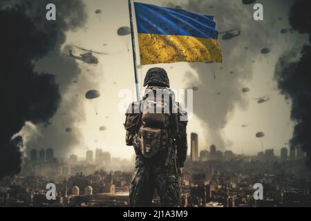 Ein ukrainischer Soldat steht mit ukrainischer Flagge in der Hand und schaut auf die zerstörte Stadt Stockfoto