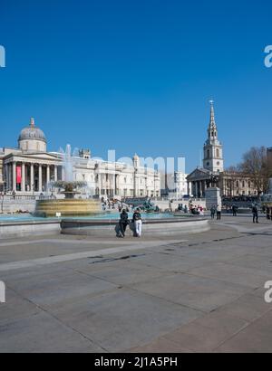 Menschen, die einen sonnigen Frühlingstag auf dem Trafalgar Square, London, England, Großbritannien, genießen möchten. Stockfoto