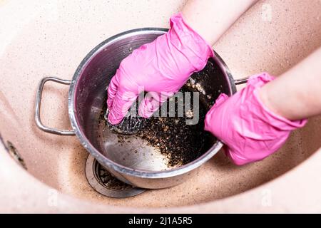 Oben Blick auf Handschuhen Wash Pfanne mit verbrannten Lebensmitteln mit Metallschwamm in rosa Waschbecken in der Küche zu Hause Stockfoto