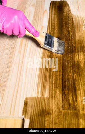 Handbezüge mit Handschuhen decken Holzbrett mit Holzfleck von Farbpinsel zu Hause Stockfoto