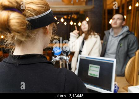 Ein Café-Mitarbeiter nimmt eine Bestellung von nicht erkennbaren Besuchern mit einem automatisierten Computersystem an. Stockfoto