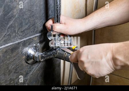 Klempner repariert alten Duschhahn an der gefliesten Wand zu Hause Stockfoto