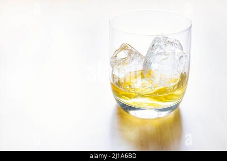 Seitenansicht des PortionsSingle Malt Scotch Whiskys auf den Felsen im Glas auf einem hellen Tisch mit Kopiefläche Stockfoto