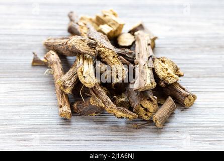 Haufen getrockneter Lakritzwurzeln schließen sich auf dem grauen Holztisch an Stockfoto