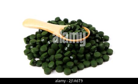 Spirulina Algentabletten mit einem Holzlöffel isoliert auf weißem Hintergrund. Nahrungsergänzungsmittel, Vitamine und Gesundheitskonzept Stockfoto