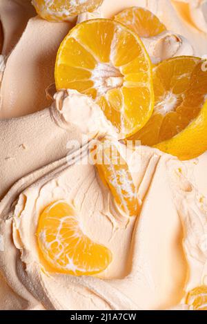 Frozen Tangerine Flavour Gelato - Vollformat Detail. Nahaufnahme einer orangefarbenen Oberflächenstruktur von Eiscreme, die mit Stücken von Mandarinenfrüchten bedeckt ist. Stockfoto