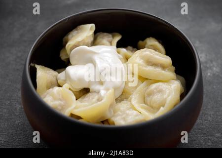 Gekochte Knödel mit Fleisch im Topf, mit saurer Rahm. Auf einem dunklen Hintergrund Stockfoto