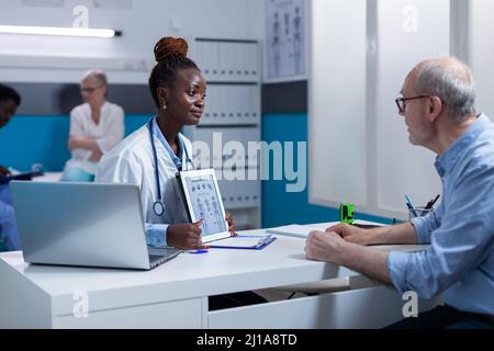 Krankenhaus orthopädischen Arzt Experte erklärt medizinische Diagramm zu kranken Rentner. Medic im Gespräch mit dem Seniorpatienten über verordnete Medizin, Beratungsergebnis und gesundheitliche Risiken von Krankheiten. Stockfoto