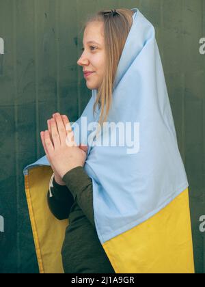 kaukasisch blonde Teenager eingewickelt in einer ukrainischen Flagge über einem neutralen Hintergrund gegen Krieg Konzept Stockfoto