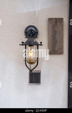 Nahaufnahme einer weißglühenden Straßenlampe, die an der Wand im Freien installiert ist Stockfoto