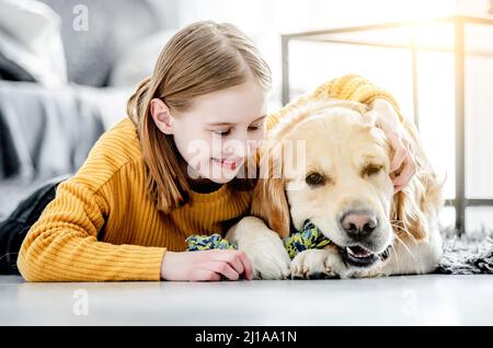 Präteen Mädchen umarmt goldenen Retriever Hund auf dem Boden liegend und lächelnd. Hübsches Kind Kind streicheln doggy Haustier zu Hause Stockfoto