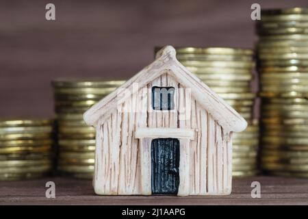 Miniatur-Holzspielzeughaus-Modell Nahaufnahme mit den Stapel von Münzen im Hintergrund. Konzept der Hypothekeneinlage. Stockfoto