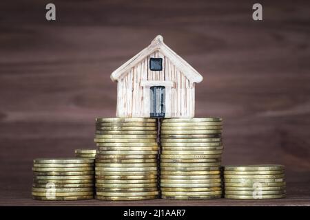 Miniatur-Holzhausmodell, das auf den Münzstapeln steht. Konzept der Hypothekeneinlage. Stockfoto