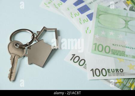 Schlüssel für ein neues Haus und Euro-Geldscheine und -Cent auf blauem Hintergrund. Nahaufnahme. Konzept teure Stromrechnungen und Hauszahlungen. Stockfoto