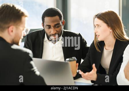 Die Chefin mit einer Kaffeetasse zeigt ihren Mitarbeitern ein Geschäftsentwicklungsmodell auf einem Laptop Stockfoto