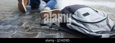 Rucksack liegt auf rutschigen Pflasterplatten in der Nähe eines herunterfallenden Mannes in der Nähe Stockfoto