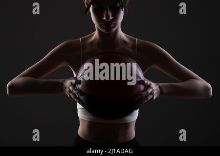 Teenager Mädchen mit Basketball. Seitlich beleuchtetes Studioporträt vor dunklem Hintergrund. Stockfoto