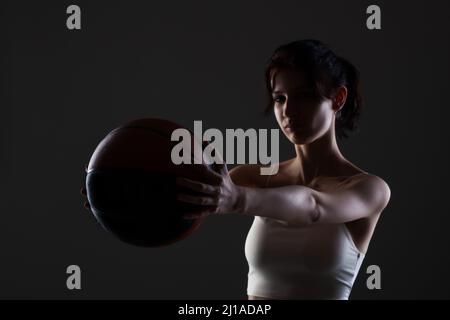 Teenager Mädchen mit Basketball. Seitlich beleuchtetes Studioporträt vor dunklem Hintergrund. Stockfoto