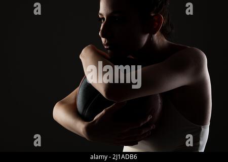 Teenager Mädchen mit Basketball. Seitlich beleuchtetes Studioporträt vor dunklem Hintergrund. Stockfoto