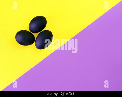 Schwarze Eier auf dem gelben und violetten Hintergrund. Ostern, Vielfalt, geometrisch, Muster, Lebensmittelkonzept Stockfoto