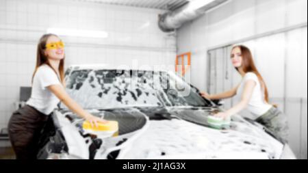 Hintergrund verschwommener Handgriff Schwamm über schwarzem Auto zum Waschen von weißem Schaum. Stockfoto