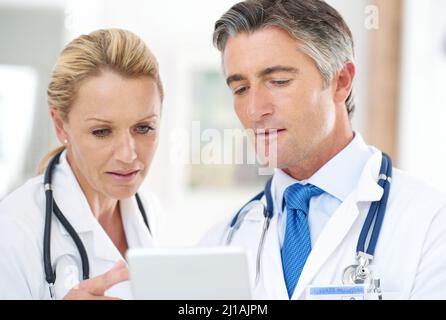 Diskussion der Diagnose. Aufnahme von zwei Ärzten, die sich über ein digitales Tablet in einem Krankenhaus unterhalten. Stockfoto