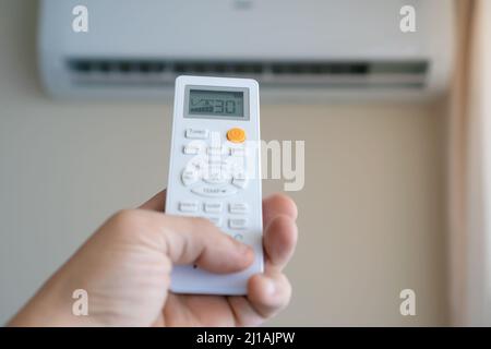 Nahaufnahme einer Männerhand, die die Fernbedienung auf eine weiße Klimaanlage an der Wand zeigt, Platz kopieren Stockfoto