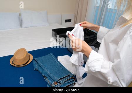 Nahaufnahme eine junge Frau in einem weißen Hemd sammelt oder packt Dinge aus einem Koffer, der auf dem Bett liegt. Konzept von Reisen, Urlaub Stockfoto