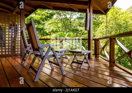 Zwei Holzstühle auf einer Holzterrasse in den Baumkronen des Morne Seychelles National Park Regenwaldes mit üppiger tropischer Vegetation und Palmen. Stockfoto