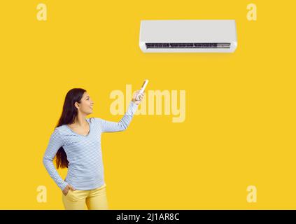 Frau mit Fernbedienung passt die angenehme Temperatur an der Klimaanlage auf gelbem Hintergrund an. Stockfoto