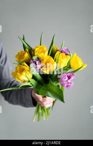 Gelbe und lila Tulpen Bouquet in den Händen über grauen Beton Wand Hintergrund. Konzept des Muttertages, Frauentag, Jahrestag, Geschenk an eine Freundin Stockfoto