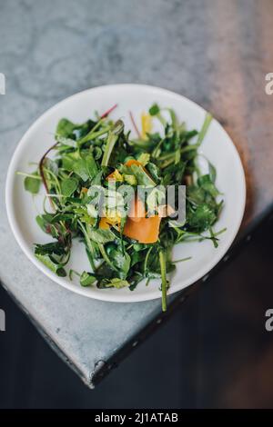 Wilder Brunnensalat mit Erbsen und Orangenmimolette im Restaurant im Freien Stockfoto